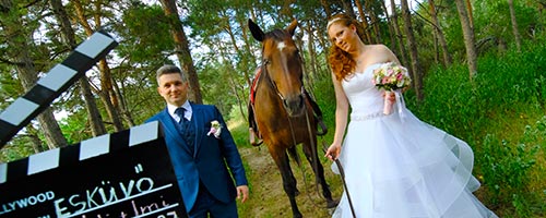 Esküvői pár erdőben egy lovet vezetve, baloldalról egy filmes csapó